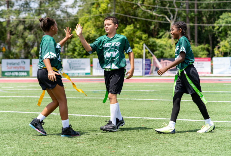Three kids high-fiving during a game of NFL flag football